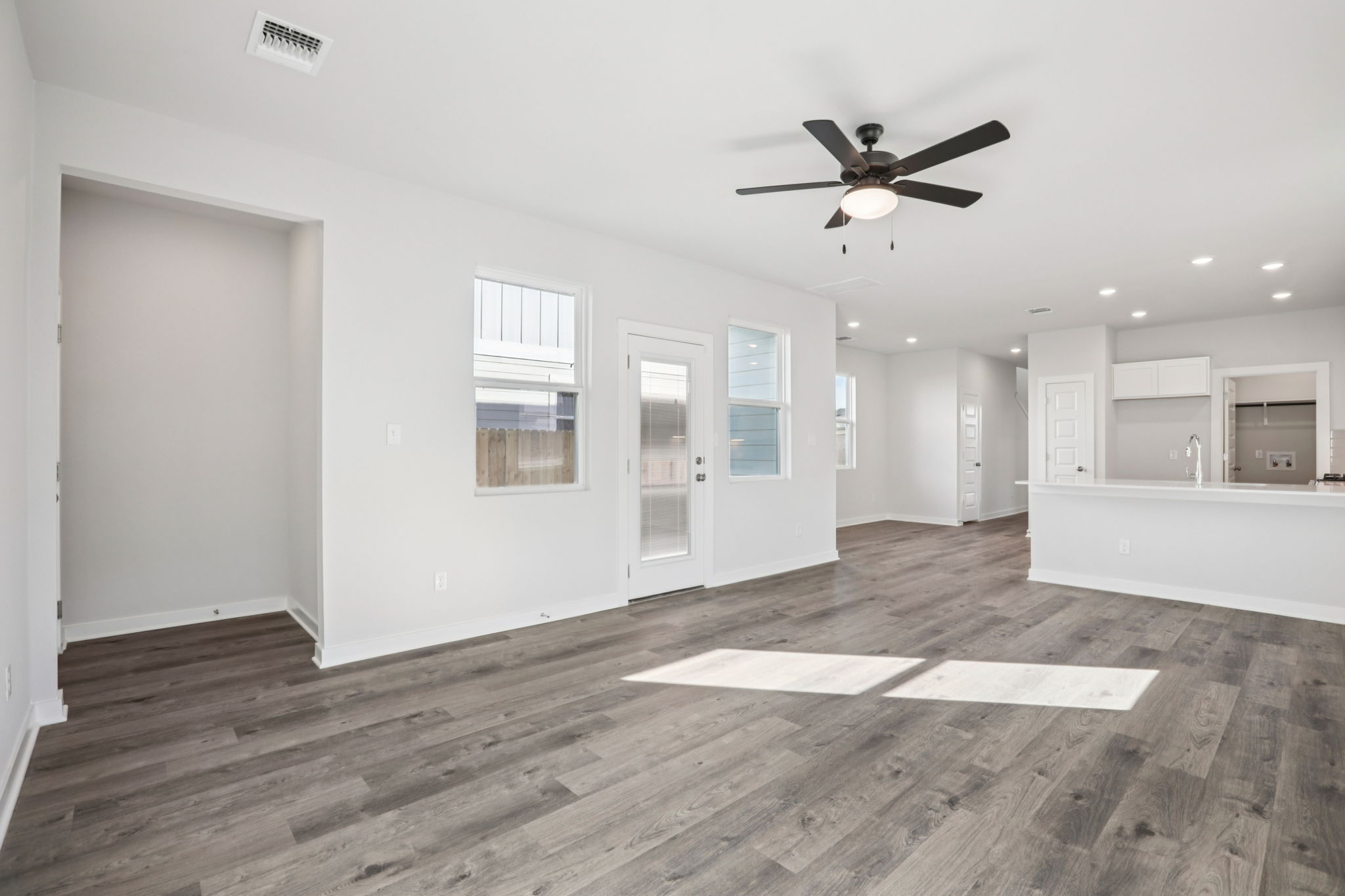 A room with white walls and a wood floor with a fan.