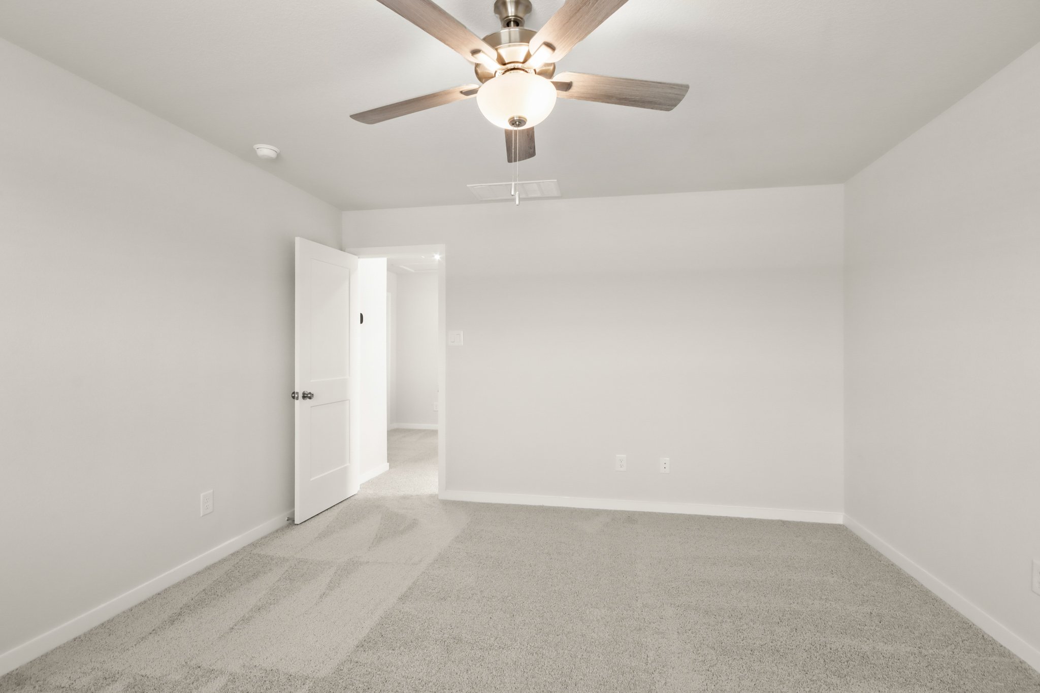A room with a ceiling fan and white walls.