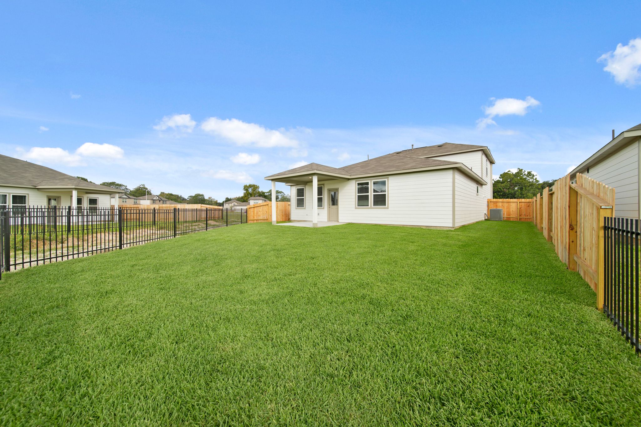 A grassy yard with a fence and houses in the background.