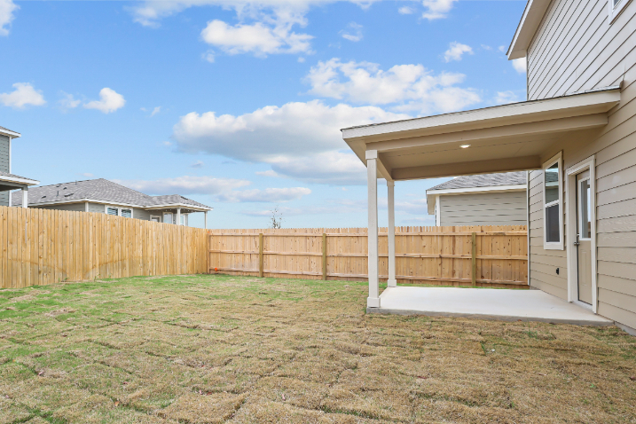 A fenced in yard with a house and a grass yard.